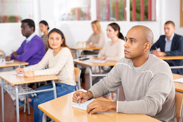 Focused adult latin american man listening to lecture in classroom with group. Postgraduate education concept