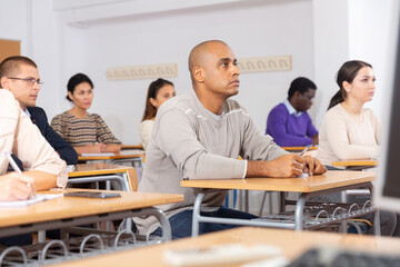 Portrait of focused young adult male studying in classroom with colleagues