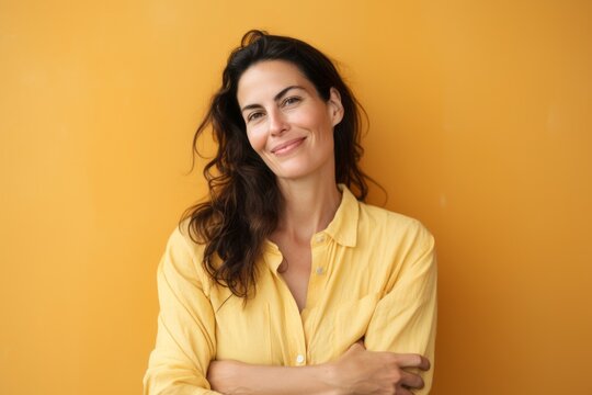 Portrait of a smiling young woman standing with arms crossed over yellow background