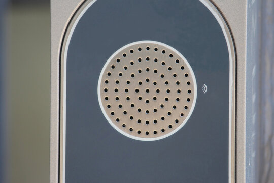 Grey circular public microphone speaker. An  emergency point speaker at a light rail station