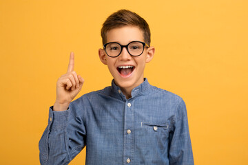 Enthusiastic teen boy wearing glasses pointing upwards with finger - obrazy, fototapety, plakaty