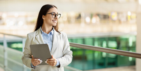 Optimistic businesswoman with glasses holding a digital tablet, looking to the side with a smile