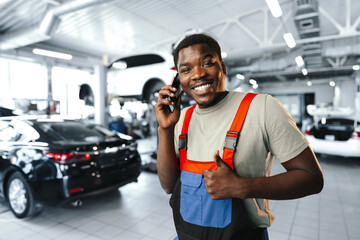 Young African mechanic man wearing uniform using mobile phone in a car service