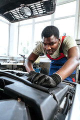 Young African man working under the hood of car fixing engine in auto service