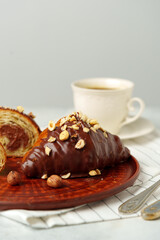 Chocolate croissant on clay plate with cup of coffee on table