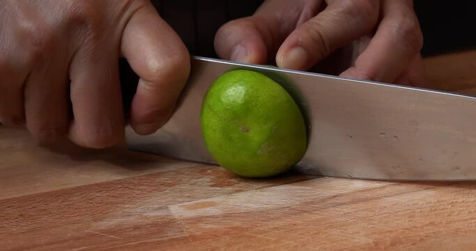 Slow Motion of a woman is cutting a half of lime wedge for cooking, preparing lime wedge for squeezing, slicing green lemon