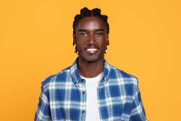 Confident young black man with braided hair posing on yellow background
