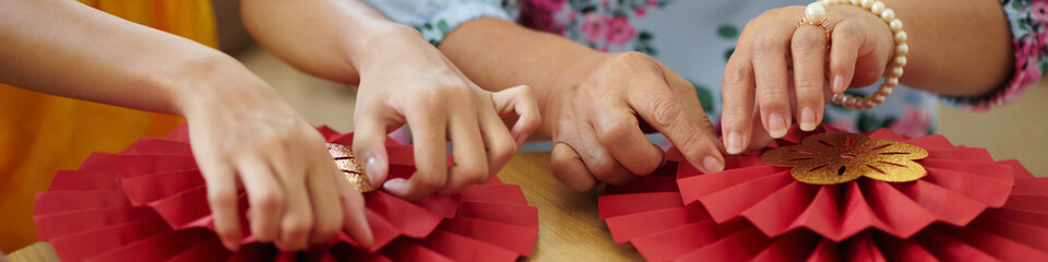 Header with hands of family members making paper fans for Tet celebration