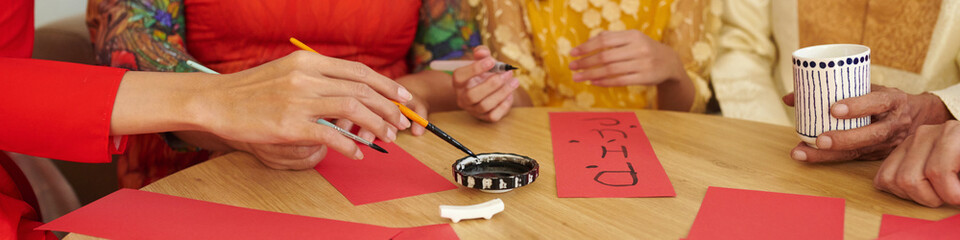 Header with hands of family members creating calligraphy couplets for Tet holiday