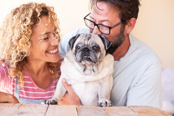 Beautiful middle aged couple man and woman in love share tender moment with their clear pug dog. Forever friends. United and happy family.