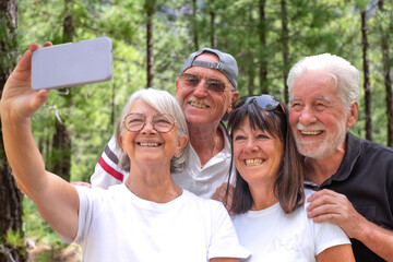 Cheerful group of senior friends enjoying retirement trekking in the forest, four elderly people take selfie with mobile phone. Sport, freedom, healthy lifestyle concept