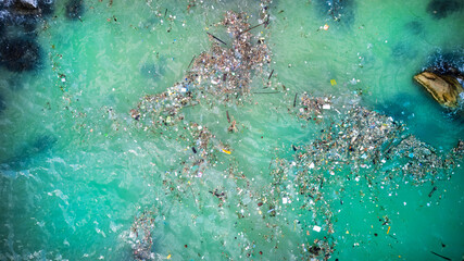 Aerial view of plastic pollution and debris floating in vibrant turquoise ocean waters,...