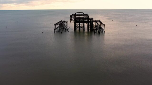 The derelict West Pier in Brighton, England. The ruined pier sits just off the popular beach. Here you can see the decaying structure as the camera approaches and tilts down on what remains.