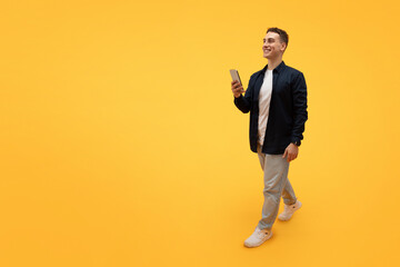 Fototapeta na wymiar Stylish young guy using smartphone, texting friends, walking on yellow