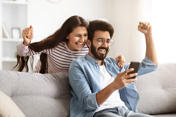 Excited millennial indian man and woman looking at phone screen