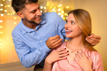 Man gifting necklace to delighted woman with glowing lights backdrop