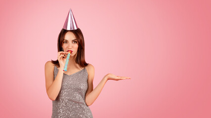 Playful woman in a sparkling dress and party hat blowing a party horn