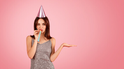 Playful woman in a sparkling dress and party hat blowing a party horn