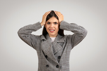 Stressed businesswoman in checkered jacket holding her head, worried expression