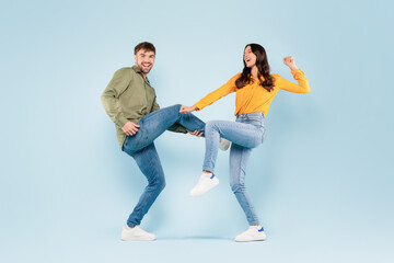 Playful couple dancing and laughing on blue background