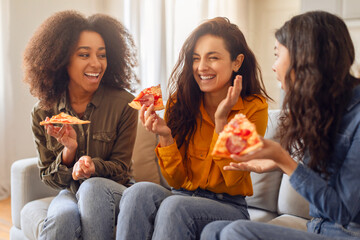 Three diverse women friends enjoying pizza and joyful chat indoors