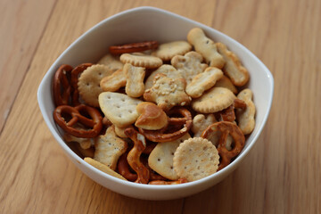 Various snack in a white bowl: pretzel with salt, crackers with seeds and herb on wooden table. Assorted party food