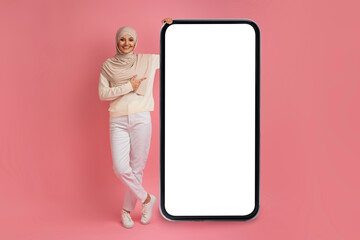 Cheerful Young Muslim Woman In Hijab Pointing At Smartphone With Blank Screen