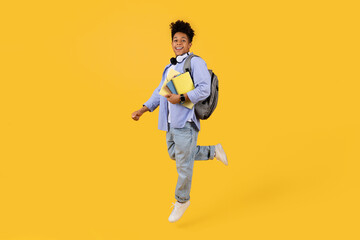 Fototapeta na wymiar Joyful black male student running with books on vibrant yellow