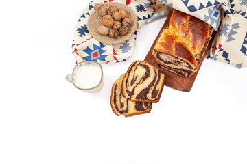 Cozonac, Romanian traditional sweet bread with walnut filling, sliced , with a glass of milk and patterned cloth, flat lay isolated