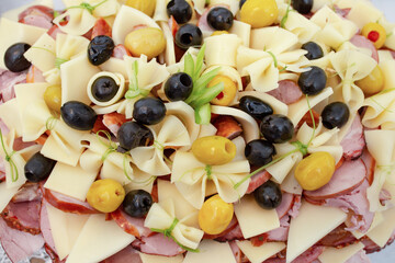 various meat products and matured cheese slices arranged,  stacked on a plate with black olives, appetizer display background, soft focus close up