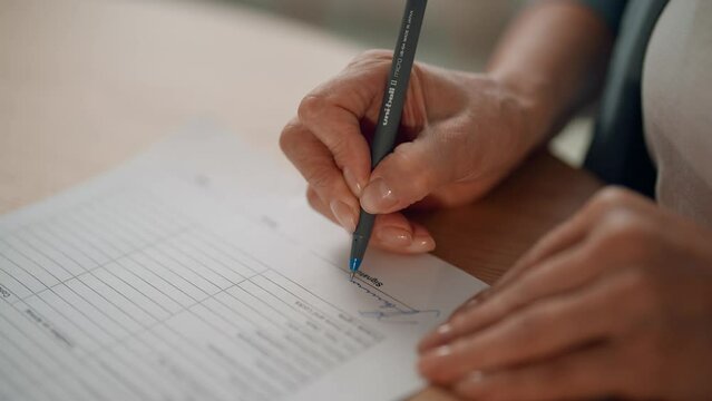 Close-up senior elderly unknown hand of businesswoman sign contract, holds pen put signature, agree with legal paper terms conditions. Make paperwork, have deal, work with documents doing job concept.