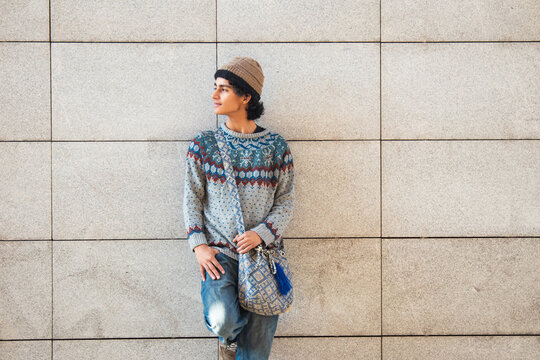 urban young man with winter clothes and bag posing on street wall