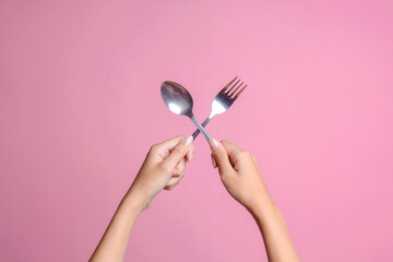 Female hands holding spoon and fork isolated on pink background