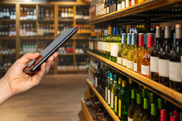 Mobile phone in female hand in front wine bottles in liquor store. Digital information about wine...
