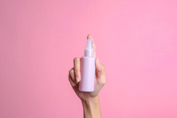 Woman hand holding small spray mockup bottle isolated on pink background