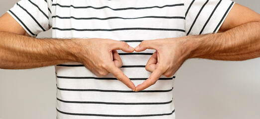 Unrecognisable male person gestures hand heart in front of his chest.