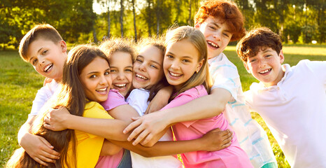 Happy children having fun on summer vacation. Group of best friends playing outdoors together. Several little kids, girls and boys with backlit hair, hugging each other tightly in a green sunny park © Studio Romantic
