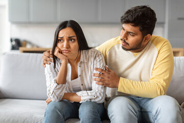 Indian man comforting his distressed girlfriend while sitting together on sofa