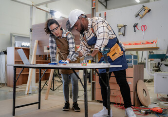 Female Latin carpenter and multiracial colleague working in carpenter's shop repair build wood...