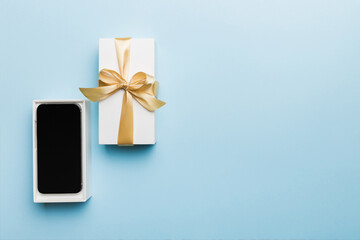 Opened gift box with gold ribbon and smartphone on color background, top view. Blank open box...