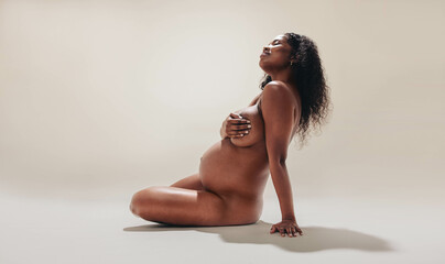 Black mother-to-be embracing her beautiful and naked pregnancy body - obrazy, fototapety, plakaty