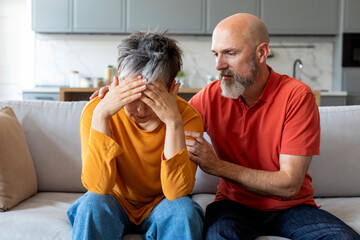 Caring elderly husband comforting his crying wife at home