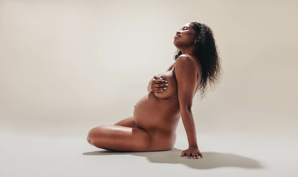 Black mother-to-be embracing her beautiful and naked pregnancy body