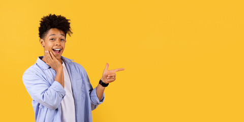 Surprised young black man pointing aside at free space on yellow background