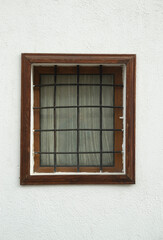Old small wooden window  with metal grill and curtain on facade