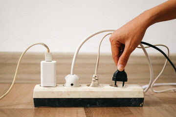 Hand holding electric plug put on multiple socket. Electrical appliances plugs full of all plugs. - obrazy, fototapety, plakaty
