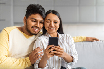 Portrait Of Happy Indian Couple Resting With Smartphone On Couch