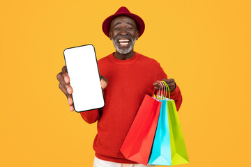 Joyful elderly black man in a red sweater and hat, showing a blank screen smartphone