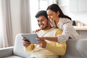 Young Happy Indian Spouses Using Digital Tablet At Home