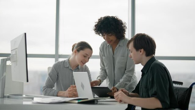 Paralyzed man works with colleagues. Guy in wheelchair has spine trauma discussing working project in office on meeting with multiethnic team women colleagues. Teamwork brainstorming, special needs.